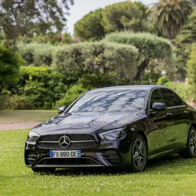 Mercedes-Benz Classe E noire garée sur une pelouse élégante. Berline premium pour un transport VIP alliant confort et raffinement avec chauffeur privé.