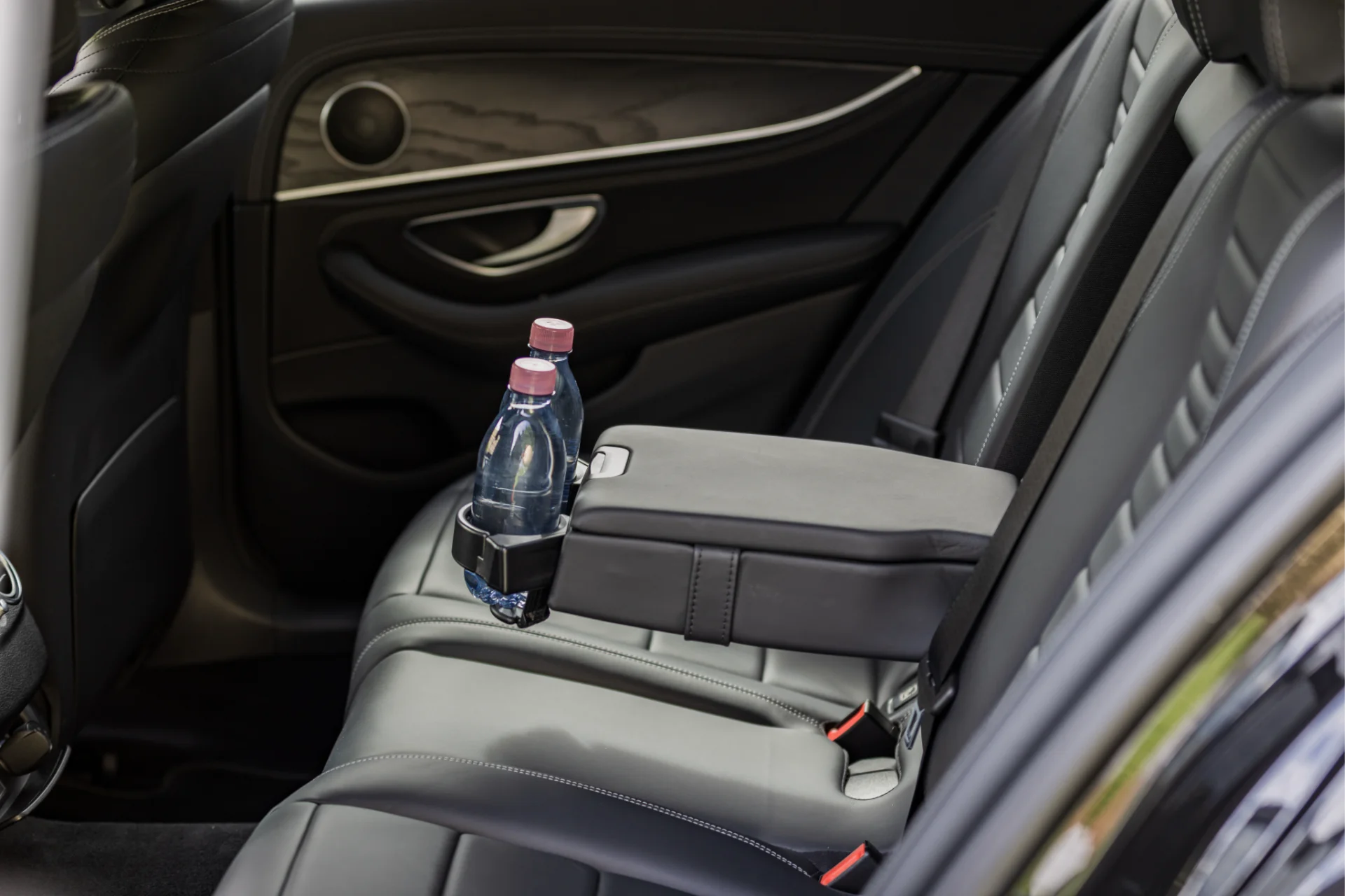 Sièges arrière confortables en cuir noir dans une Mercedes-Benz Classe E avec accoudoir central et rafraîchissements intégrés, idéal pour un voyage relaxant et élégant.