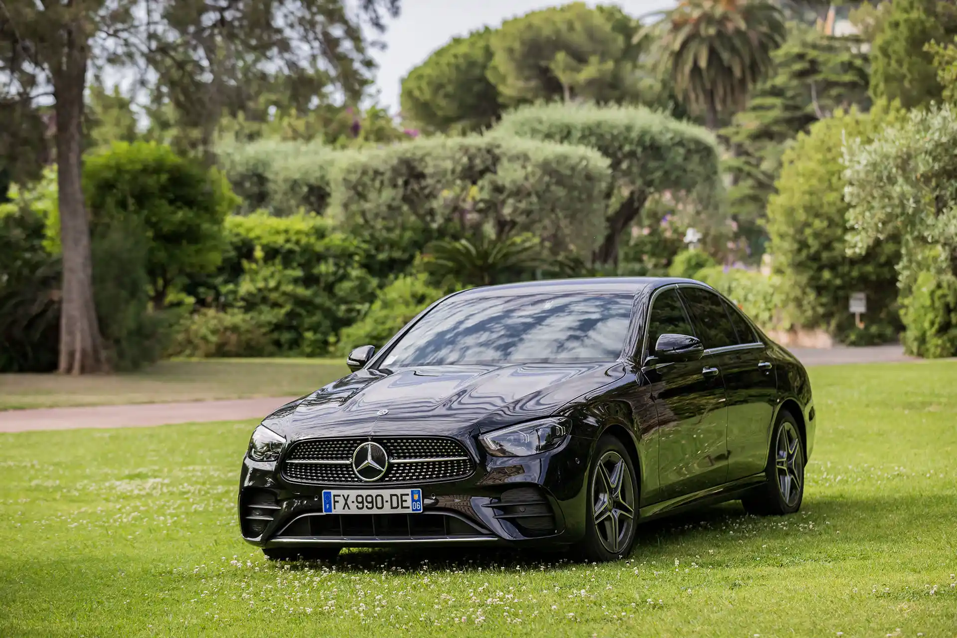Mercedes-Benz Classe E noire garée sur une pelouse élégante. Berline premium pour un transport VIP alliant confort et raffinement avec chauffeur privé.