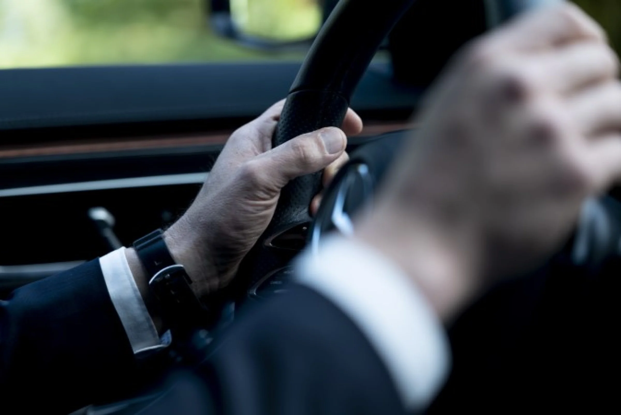 Vue rapprochée d’un chauffeur en costume tenant le volant d’un véhicule de luxe, incarnant la précision, la fiabilité et l’élégance du service de transport privé.