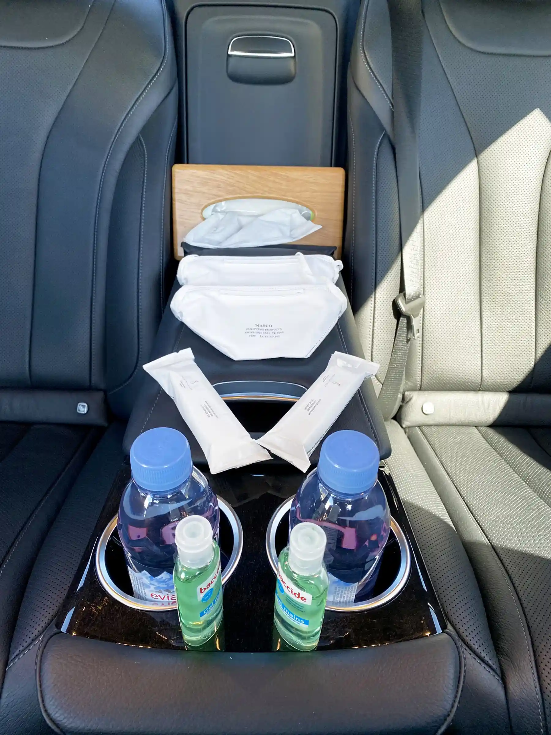 Kit sanitaire complet avec masques, lingettes, gel hydroalcoolique et bouteilles d’eau minérale à bord d’une voiture de luxe – mesures d’hygiène et confort premium pour passagers.