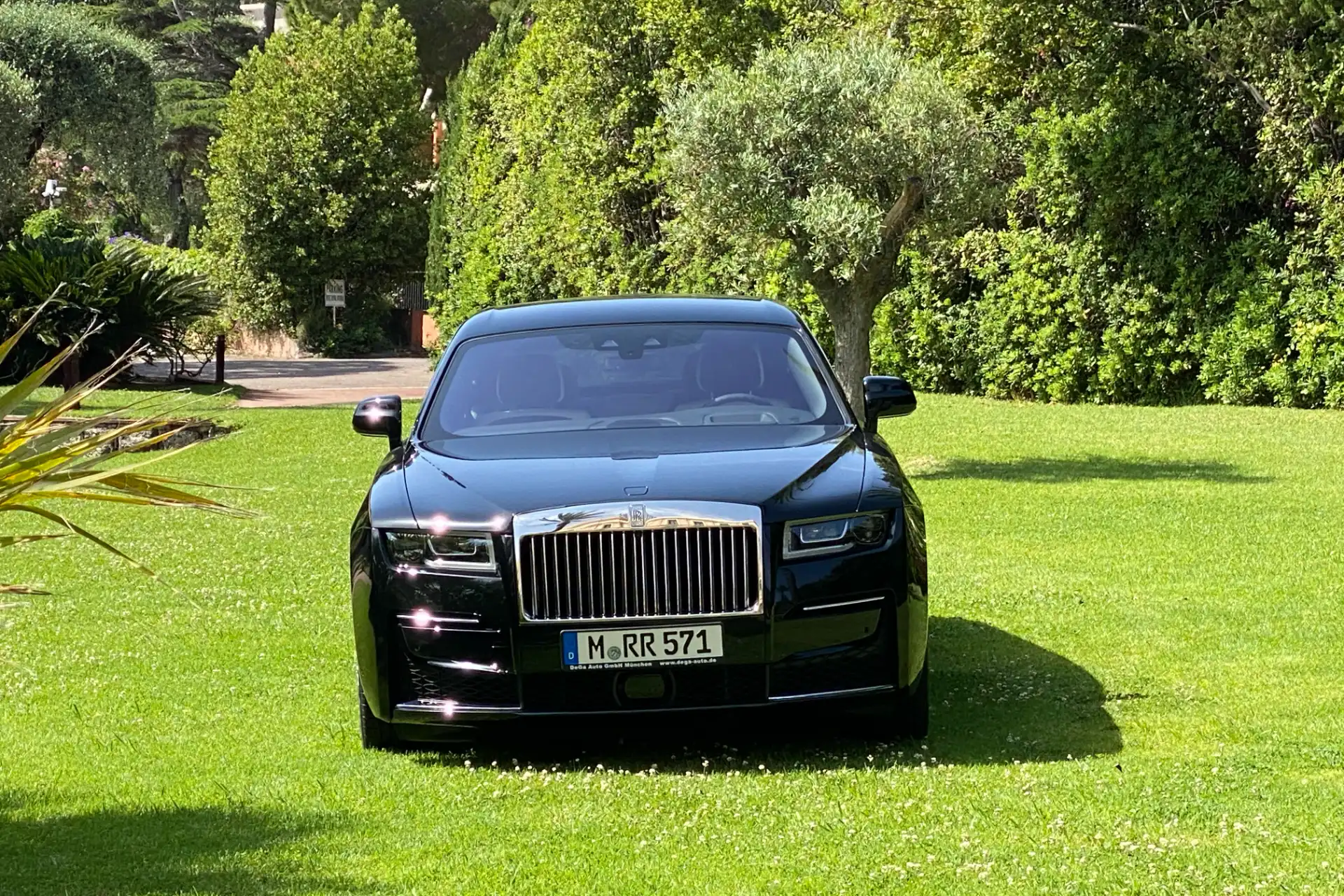 Black Rolls-Royce seen from the front, parked in a garden. Imposing grille, rectangular headlights, German license plate visible.