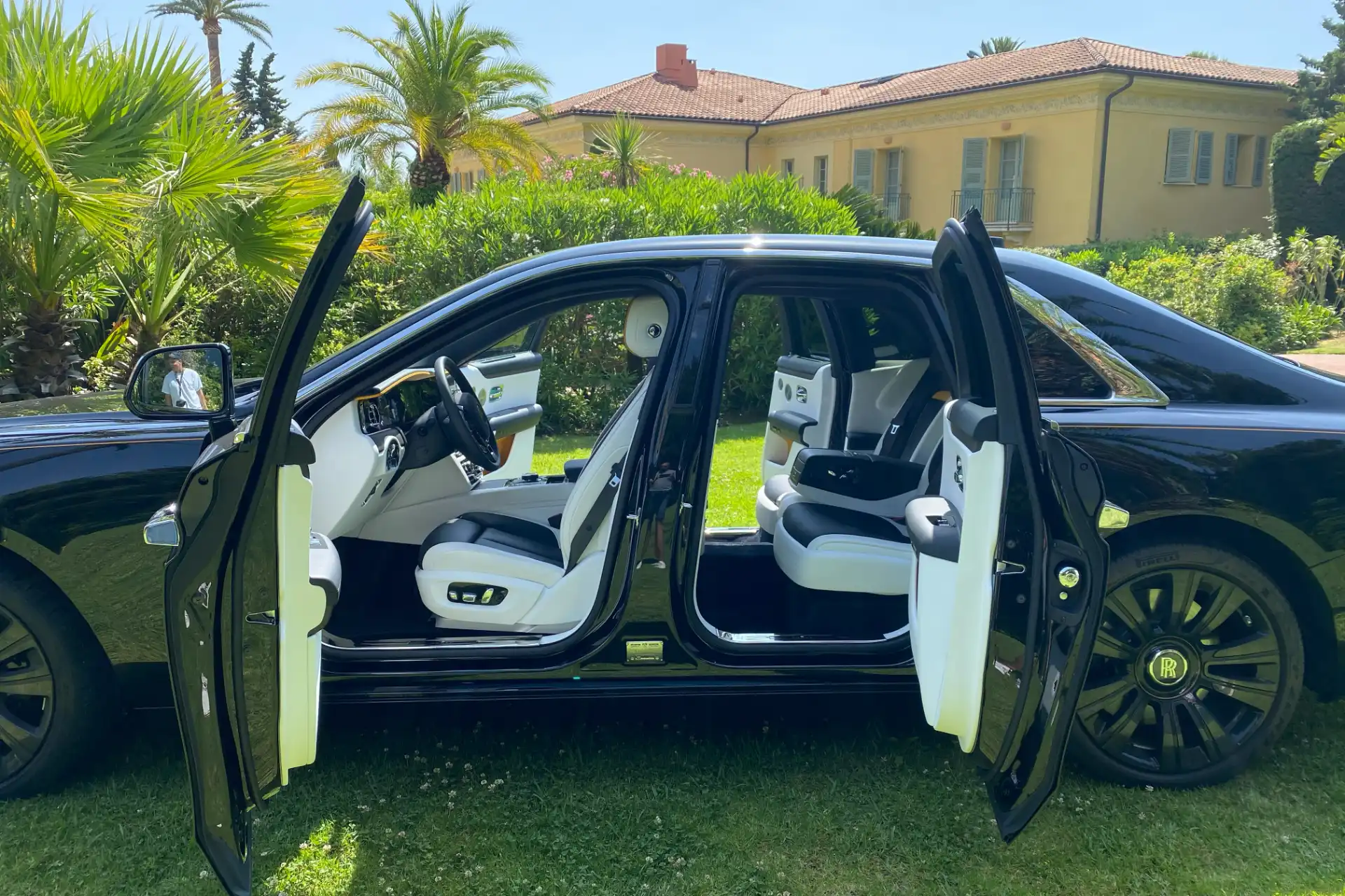 Black Rolls-Royce with doors open, side view. Black and white interior visible, rear configuration with individual seats, green residential environment.
