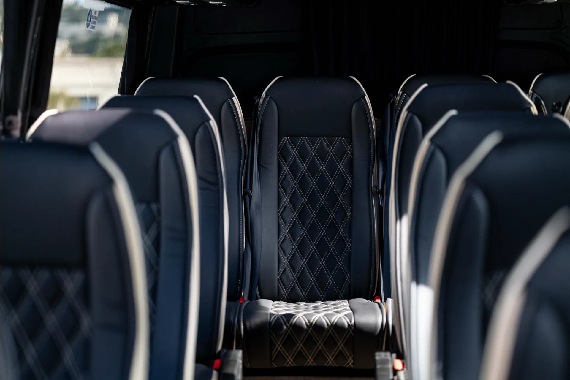 Close-up view of passenger seats in black leather with a quilted pattern. Integrated headrests and foldable armrests. Dark background of the passenger compartment.