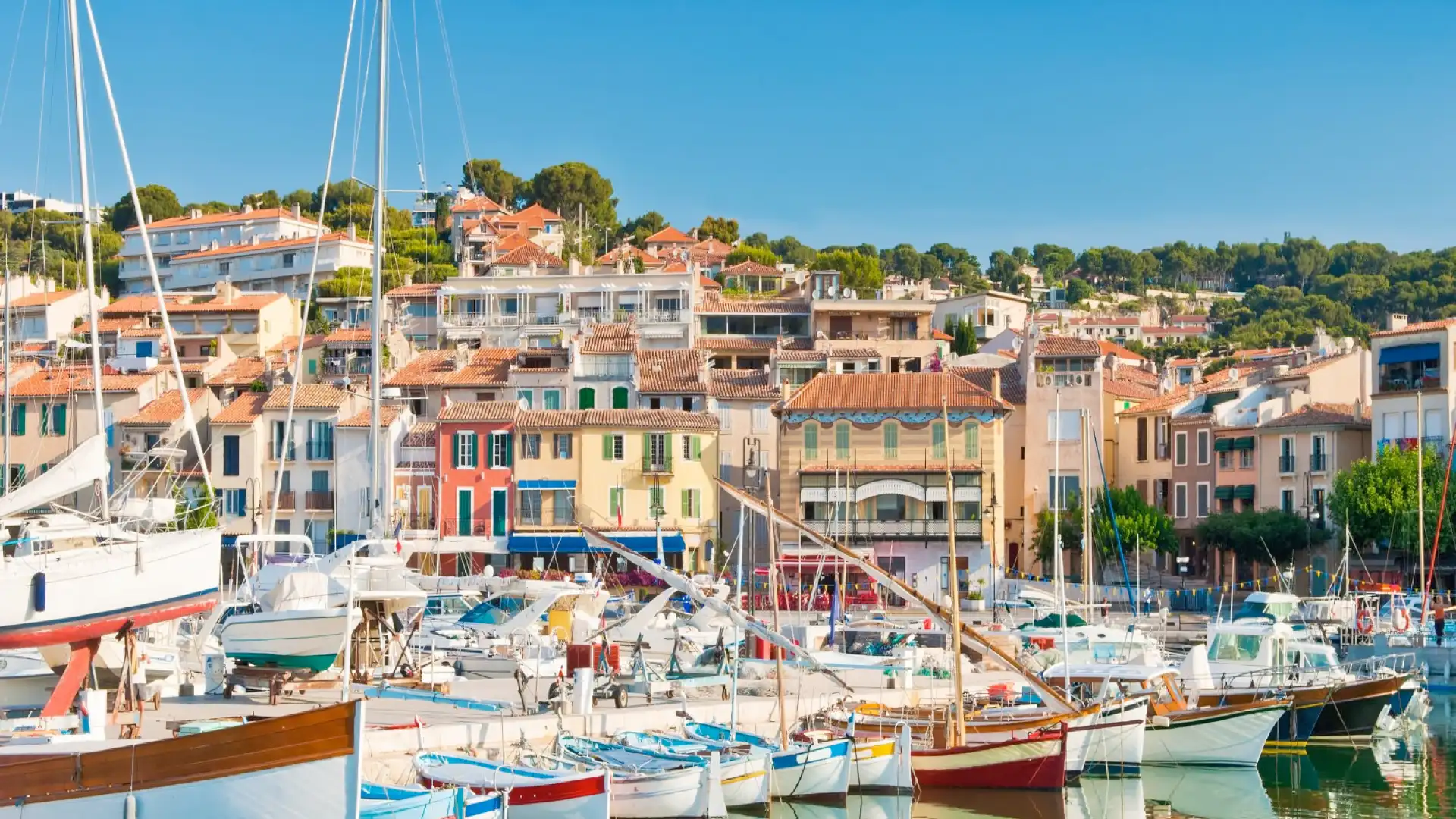 Marina with moored boats in front of colorful houses with tiled roofs in a Mediterranean coastal village, sunny tourist destination on the French Riviera.